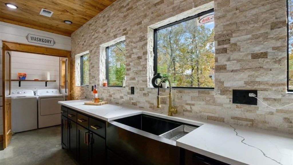 Bright kitchen with stone walls, black cabinets, and laundry area.