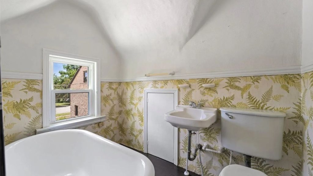Small attic bathroom with fern wallpaper and a soaking tub.