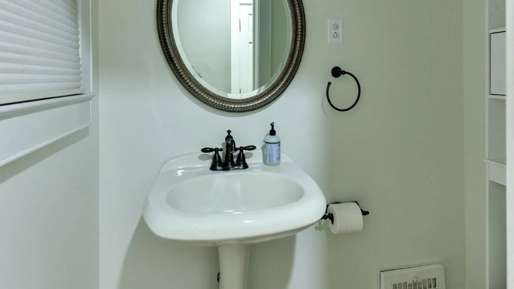Small bathroom with a pedestal sink, round mirror, and bronze fixtures.