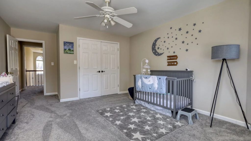 Nursery with a moon and stars theme, gray crib, and soft carpeted flooring.
