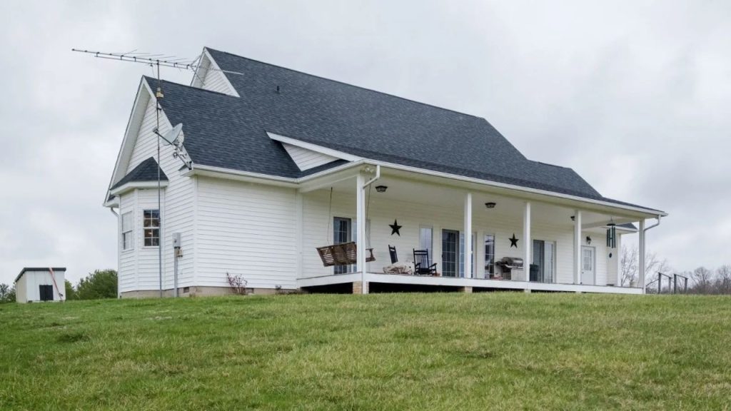 A cozy country home with a spacious porch, wooden swing, and rocking chairs overlooking an open landscape.
