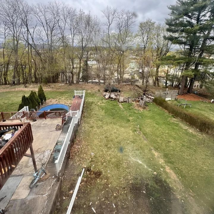 A green backyard with a deck, pool, and trees under a cloudy sky.