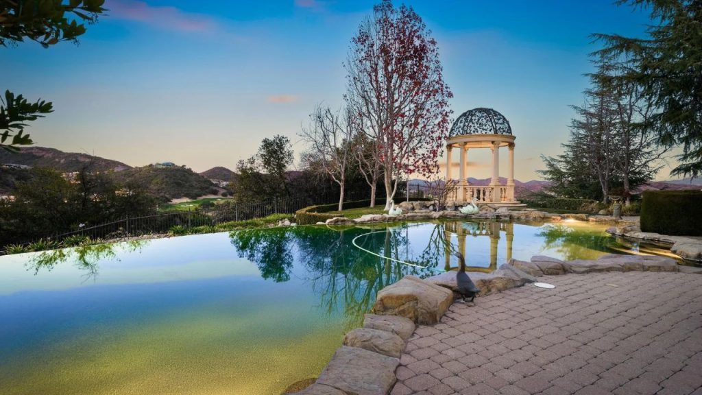 A tranquil pool with a gazebo, swans, and scenic hills at sunset.