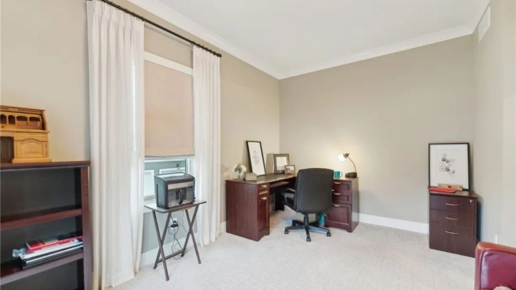 A quiet home office with a wooden desk, shelves, and large windows.