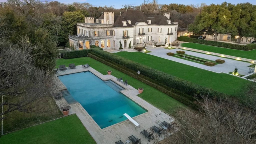 A grand estate with a pool, lush lawns, and elegant architecture at dusk.