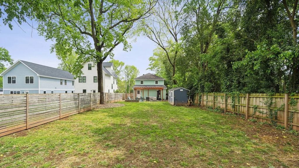 A spacious backyard with a lawn, pergola, and fire pit surrounded by trees.
