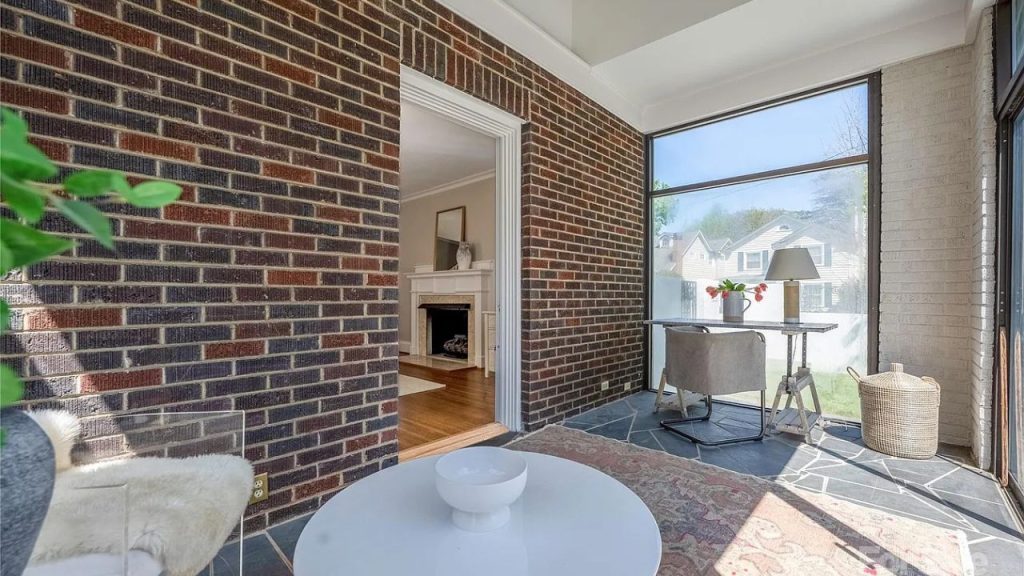 A bright sunroom with large windows, a round table, and a brick wall.