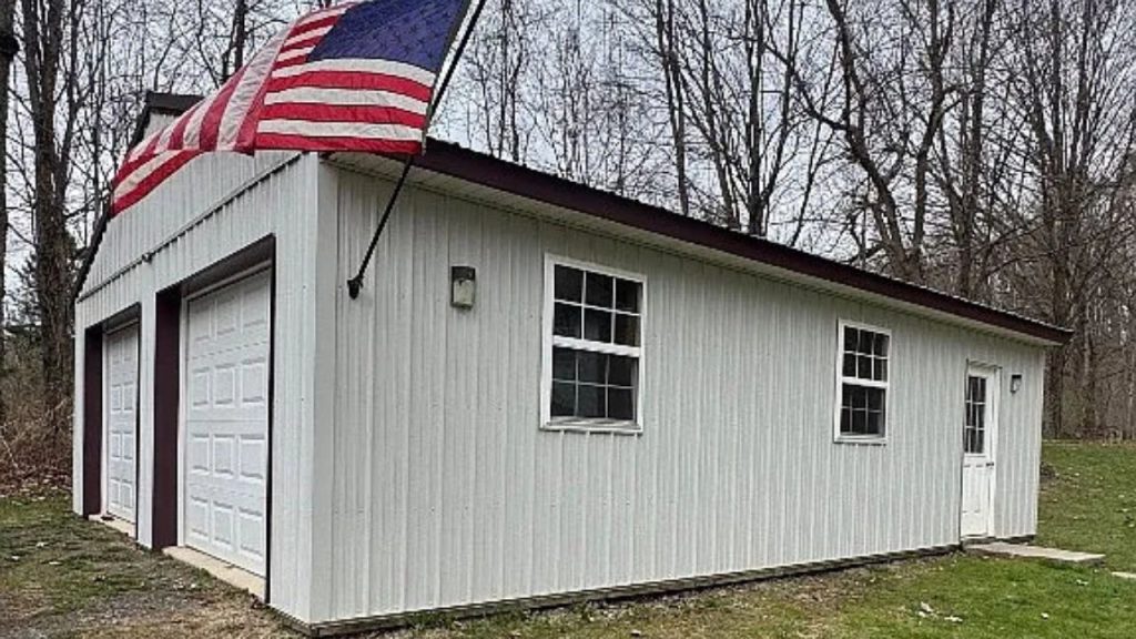 A country garage with a waving American flag, double doors, and a wooded backdrop.