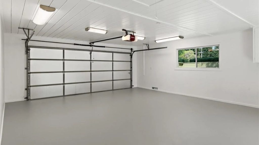 A spacious garage with a large door, bright lights, and a small window overlooking greenery.