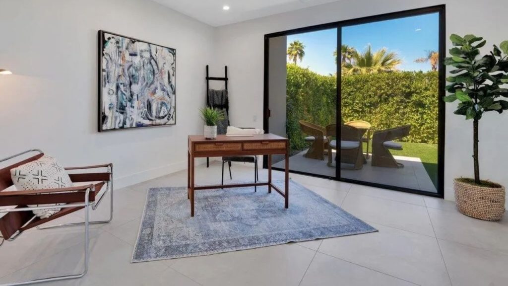 A cozy home office with a wooden desk, blue rug, and patio view.