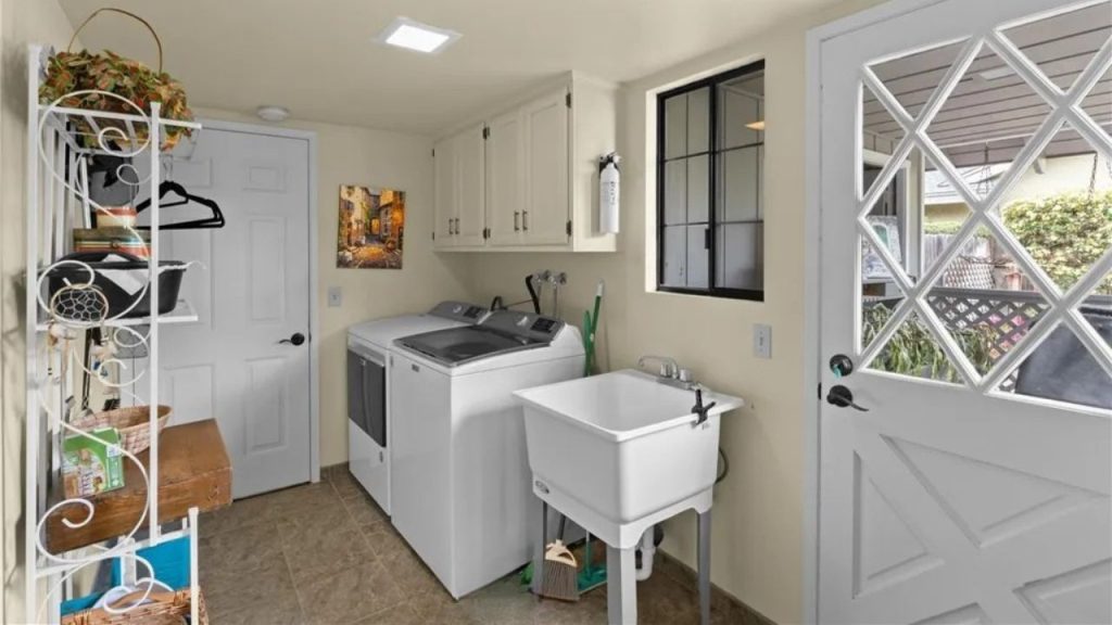 A cheerful laundry room with white appliances, utility sink, and a decorative plant shelf.