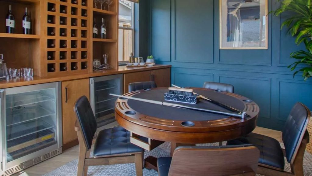 A cozy game room with a round poker table, leather chairs, wooden wine storage, and a lush green plant.