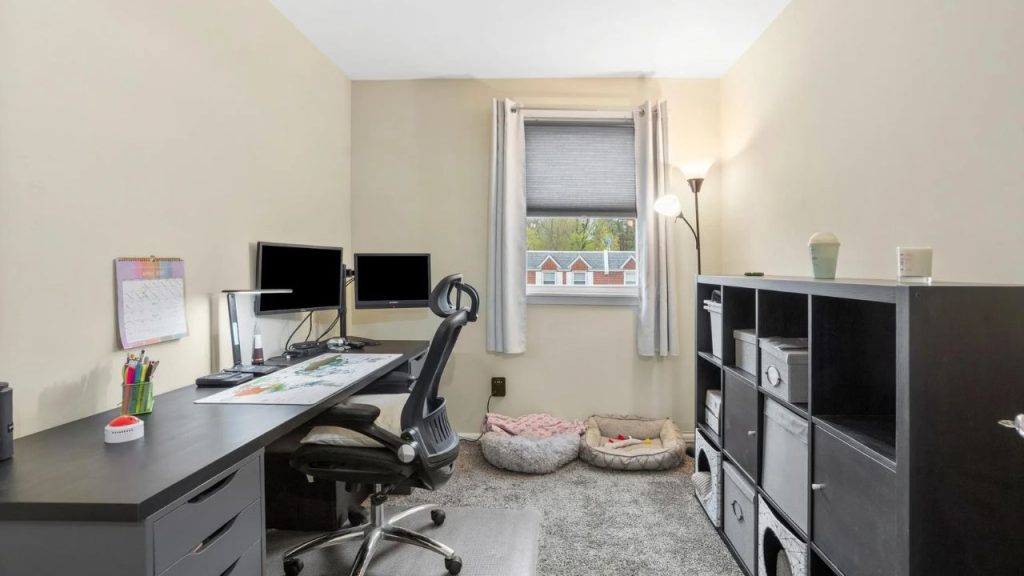 Bright home office with dual monitors, shelving, and pet beds near a window.