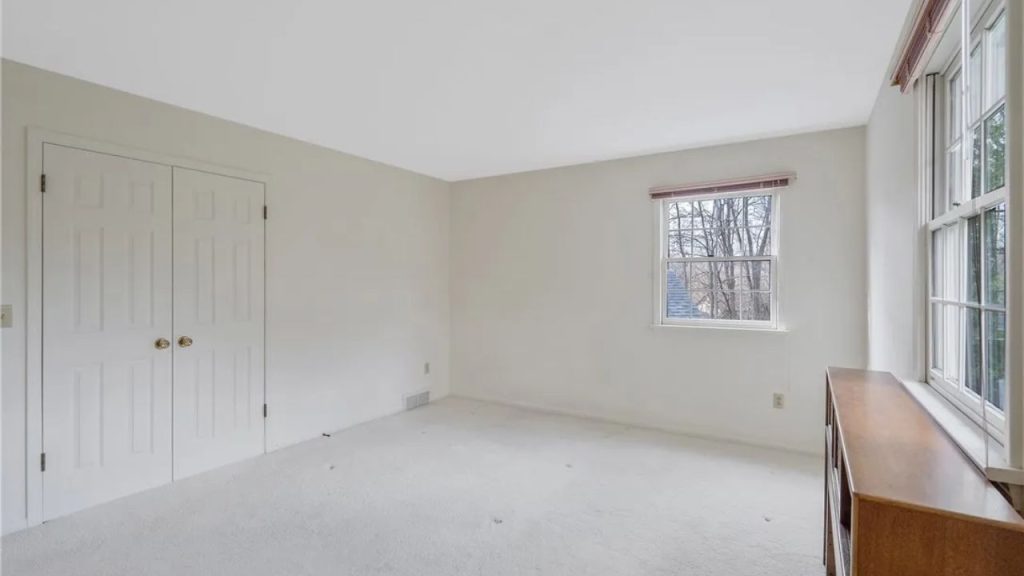 Light-filled corner bedroom with two windows and neutral carpet.
