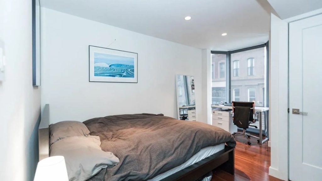 Bright bedroom with platform bed and corner desk near large windows.