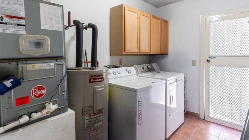 A laundry room with a washer, dryer, water heater, wooden cabinets, and a screen door.