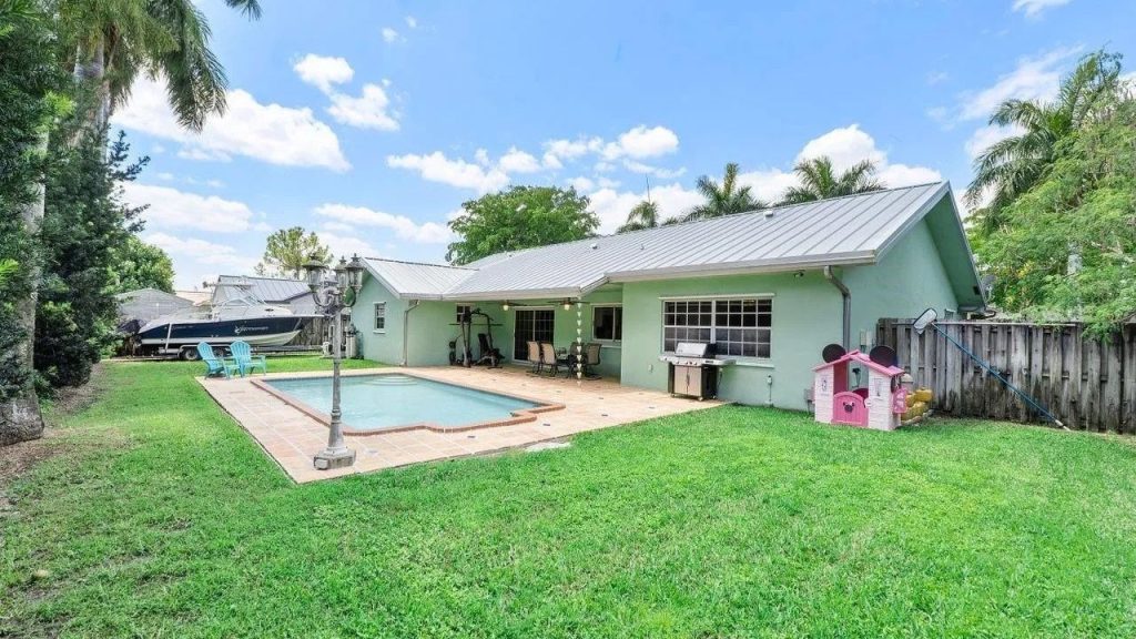 A vibrant backyard with a pool, green house, patio, and playhouse.
