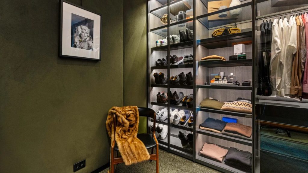 Modern walk-in closet with lit shelves and a cozy chair.

