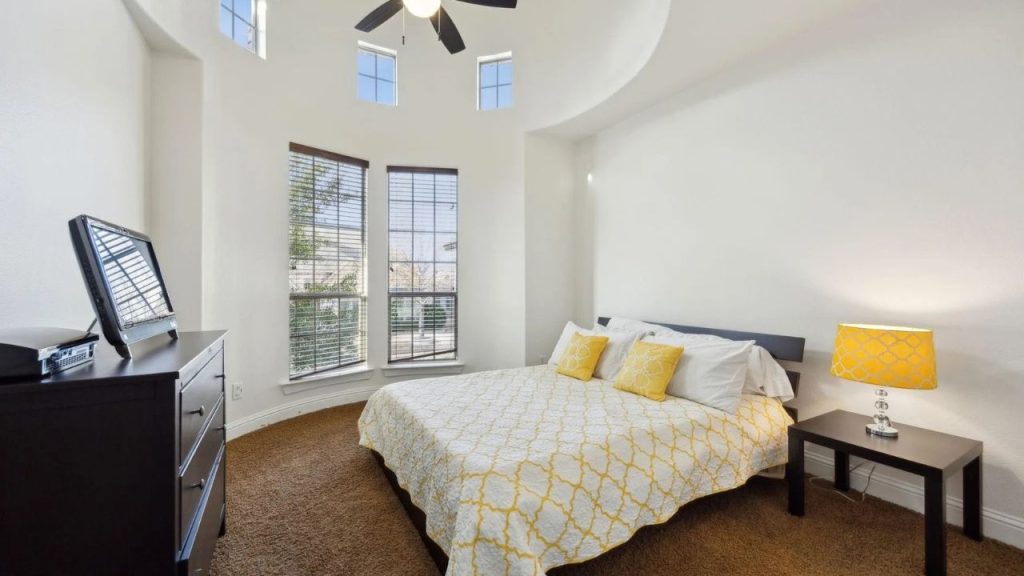 Sunny bedroom with vaulted ceiling, yellow accents, and corner windows.