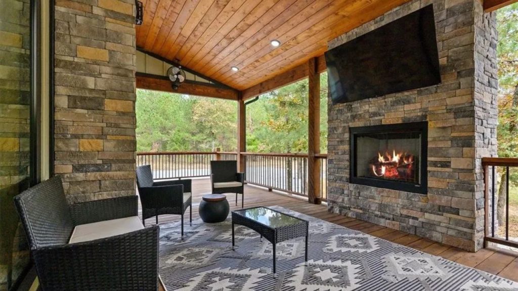 Cozy covered patio with fireplace, TV, and forest views.
