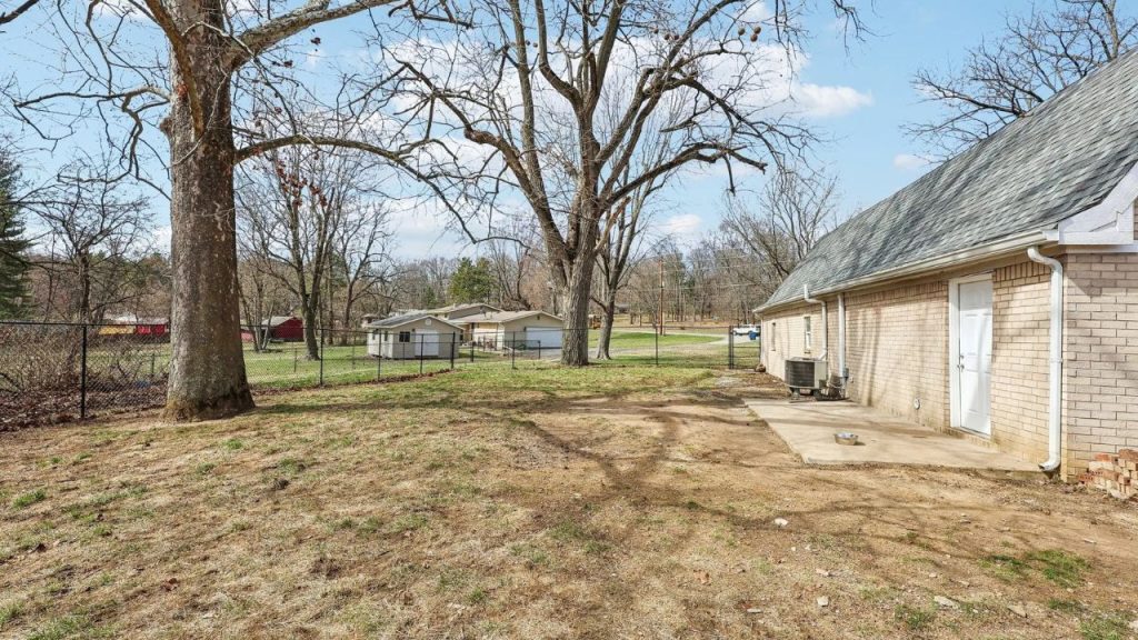 Open backyard with large trees, fenced lawn, and concrete patio.