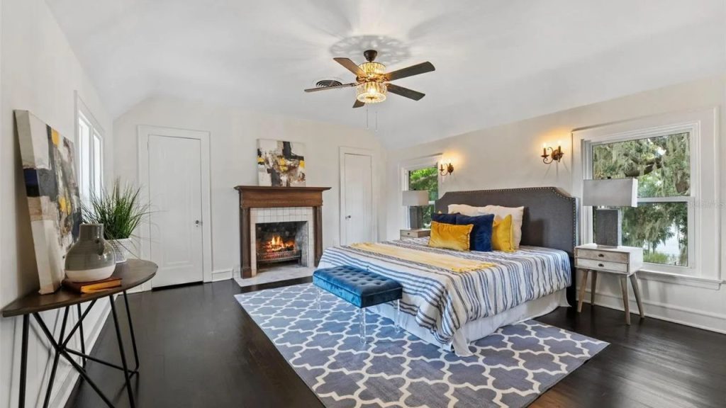 Bright bedroom with fireplace, dark floors, and lake views.