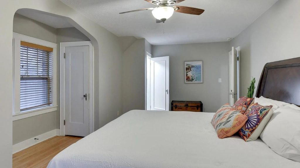 Bright bedroom with white bedding, colorful pillows, and a ceiling fan.