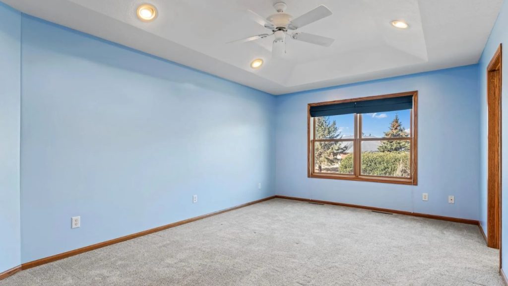 Light blue bedroom with tray ceiling and large window.
