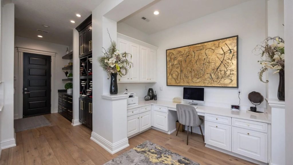 A stylish office with a white desk, gray chair, tall cabinets, and gold artwork, offering a cozy and creative workspace.