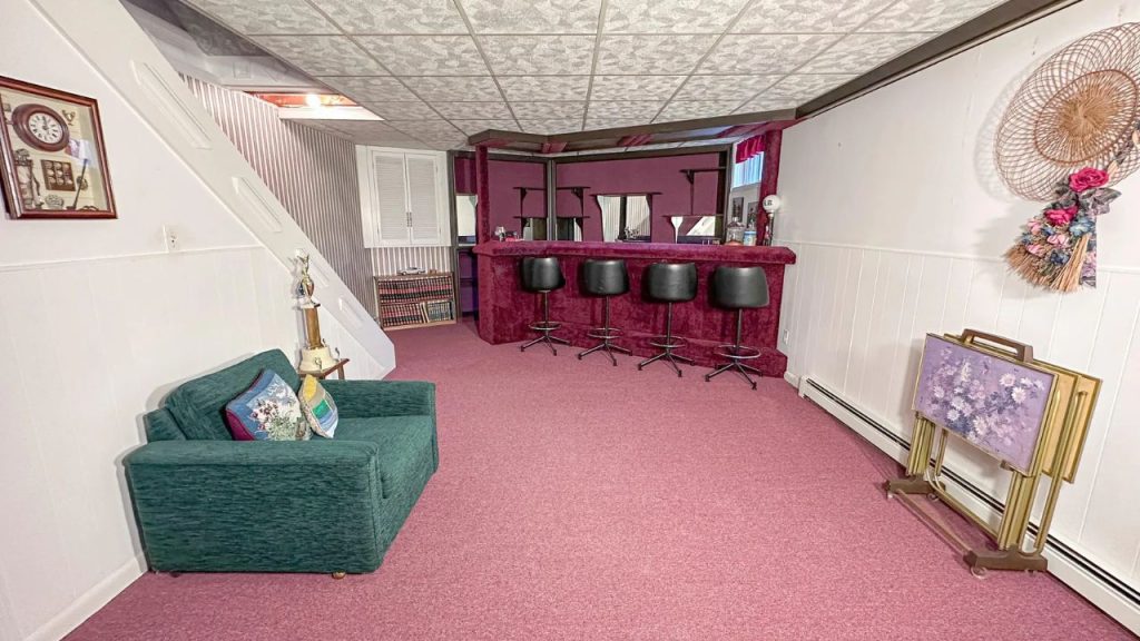 Basement bar area with burgundy counters, black stools, and green armchair.