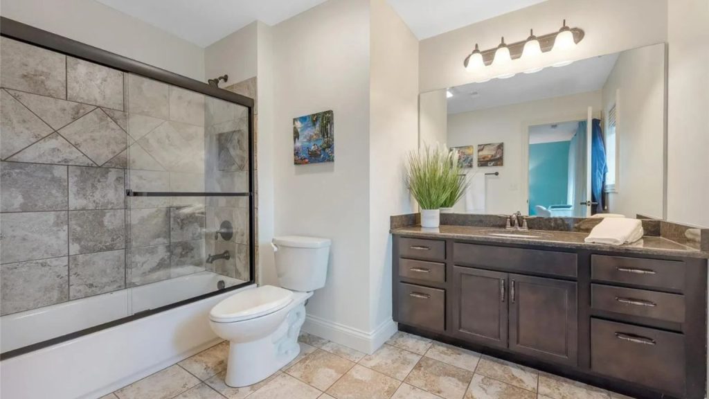 Elegant bathroom with a dark wood vanity, granite countertop, glass shower-tub, and warm lighting.