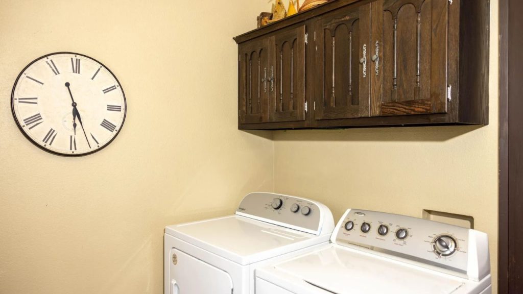 Cozy laundry room with a washer, dryer, wooden cabinets, and a vintage wall clock.