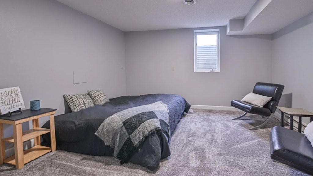 Minimal basement bedroom with dark bedding and cozy seating.