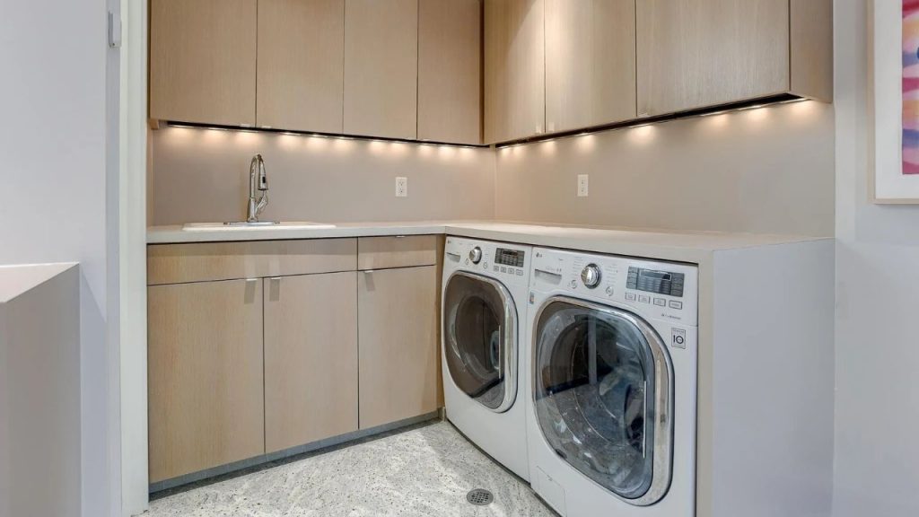 Modern laundry room with soft wood cabinets and side-by-side washer-dryer.