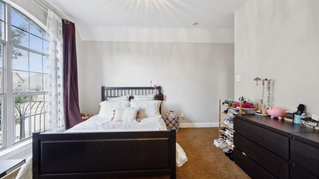 Bedroom with large arched window, white bedding, and simple furniture.