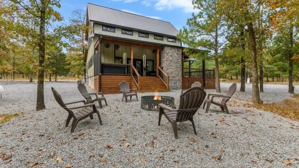 Cabin with fire pit and Adirondack chairs in wooded setting.