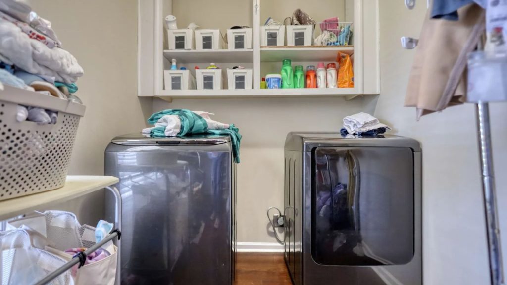 Small laundry room with modern machines and overhead shelves.