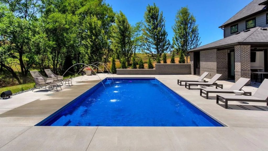 A serene backyard pool with clear blue water, lounge chairs, and lush trees, offering a tranquil and inviting escape.