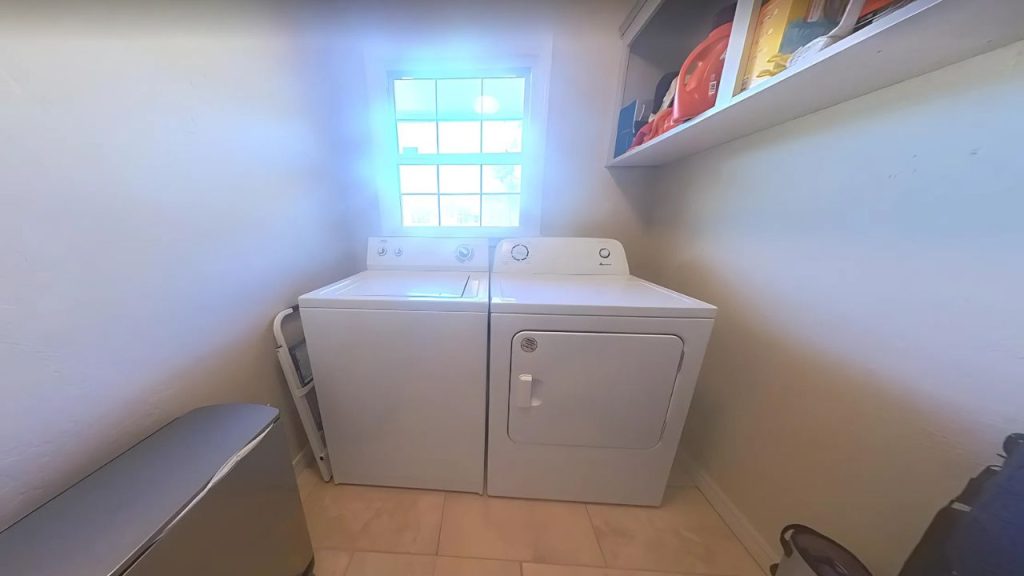 Compact laundry room with washer, dryer, and upper shelf in bright light.