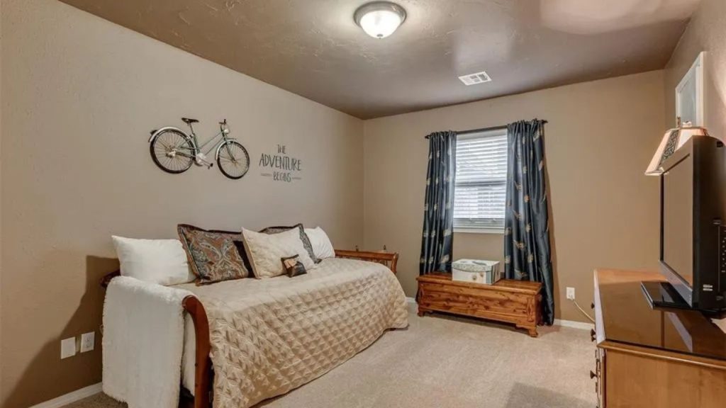 Bright kid’s room with a daybed, bicycle decor, and TV, featuring soft carpet and blue curtains.