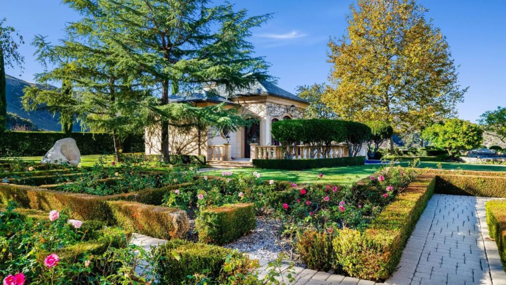 A lush garden with a pavilion, rose bushes, and scenic hills.