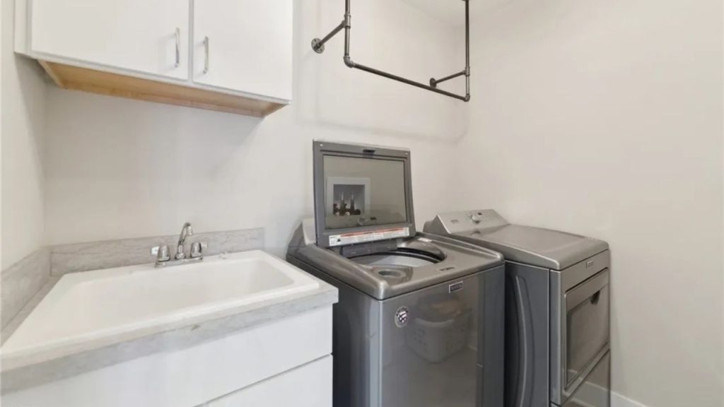 A functional laundry area with a sink, washer, dryer, and overhead rack.