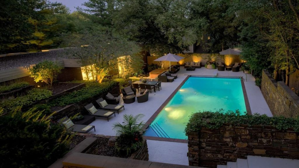 Glowing pool at dusk surrounded by trees, loungers, and cozy seating areas.
