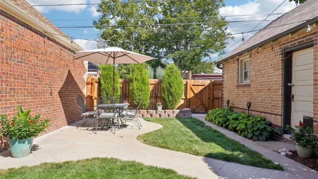 Backyard patio with dining set, umbrella, and lush greenery.