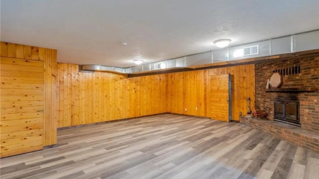 Finished basement with wood-paneled walls, gray flooring, and brick fireplace.