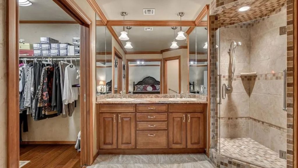 Warm-toned bathroom with double vanity, tiled shower, and walk-in closet access.