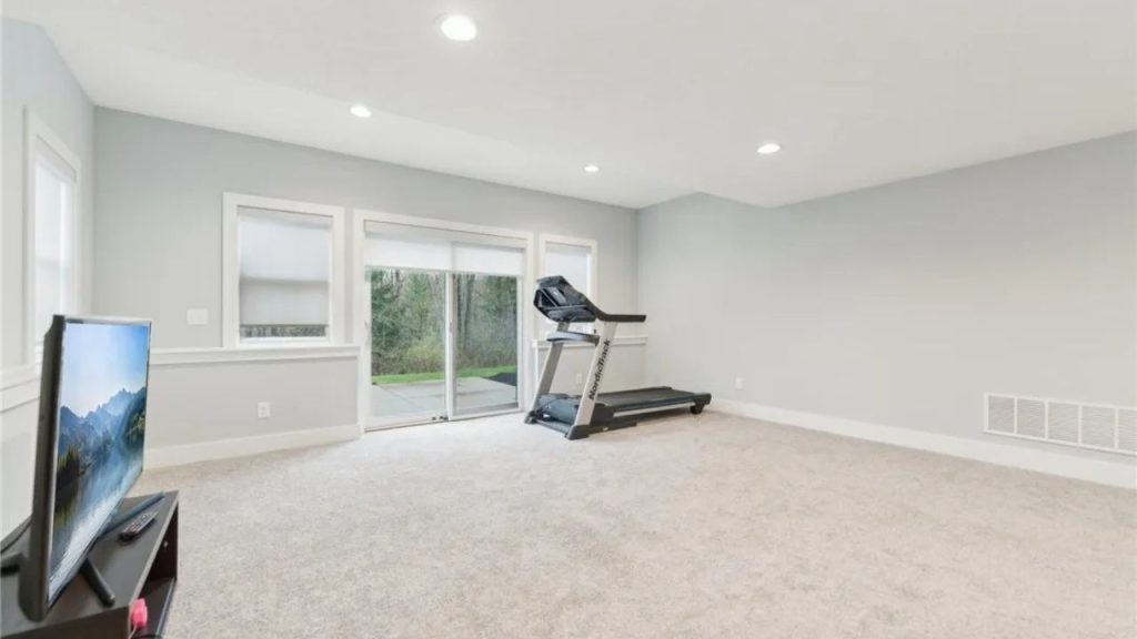 A bright workout room with a treadmill, TV, and large windows.