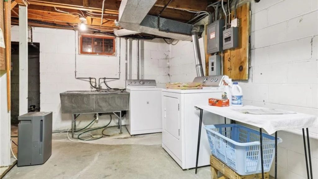 Basement laundry room with utility sink and exposed pipes.