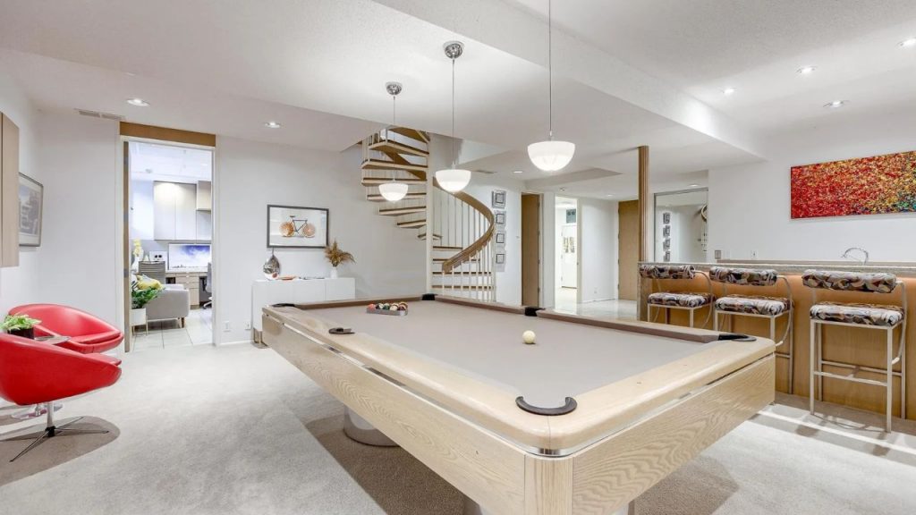 Bright game room with pool table, spiral staircase, and bar seating.