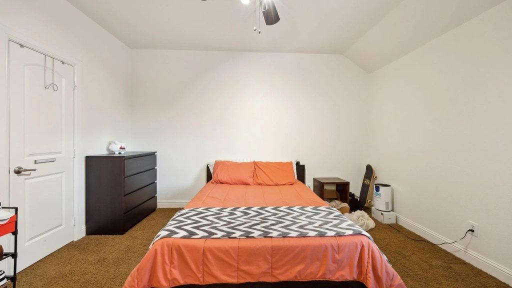 Bedroom with orange bedding, dark furniture, and a skateboard against the wall.